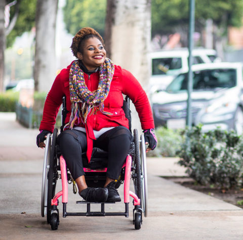 cheerful-young-black-woman-in-wheelchair-on-sidewalk-962x950