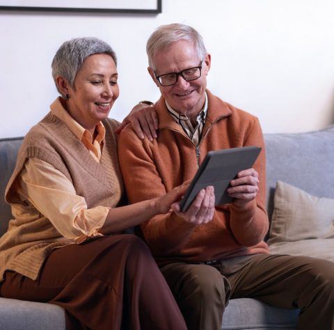 happy-senior-couple-looking-at-tablet-on-couch